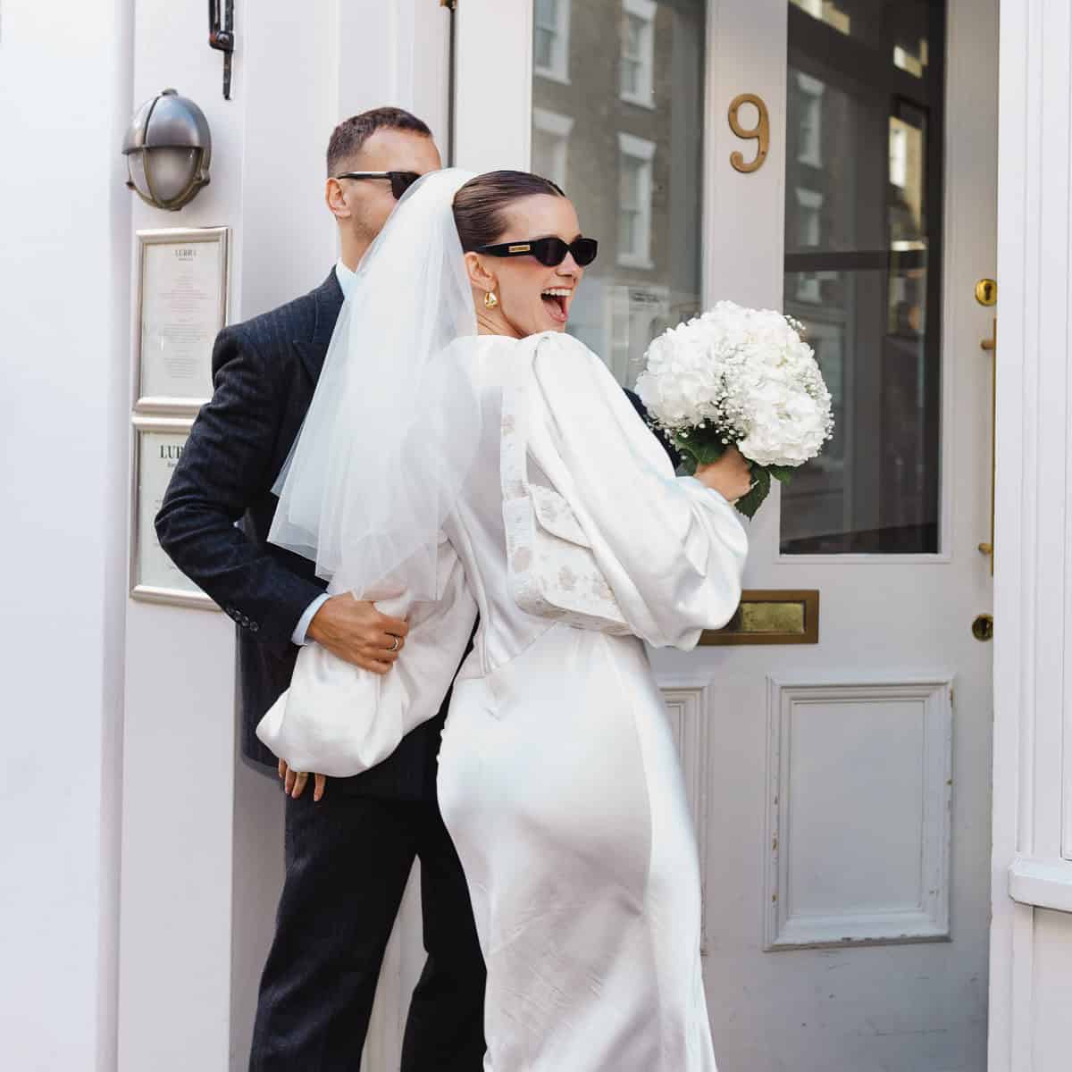 Newlywed couple wearing sunglasses entering a restaurant reception in London after their registry office wedding.