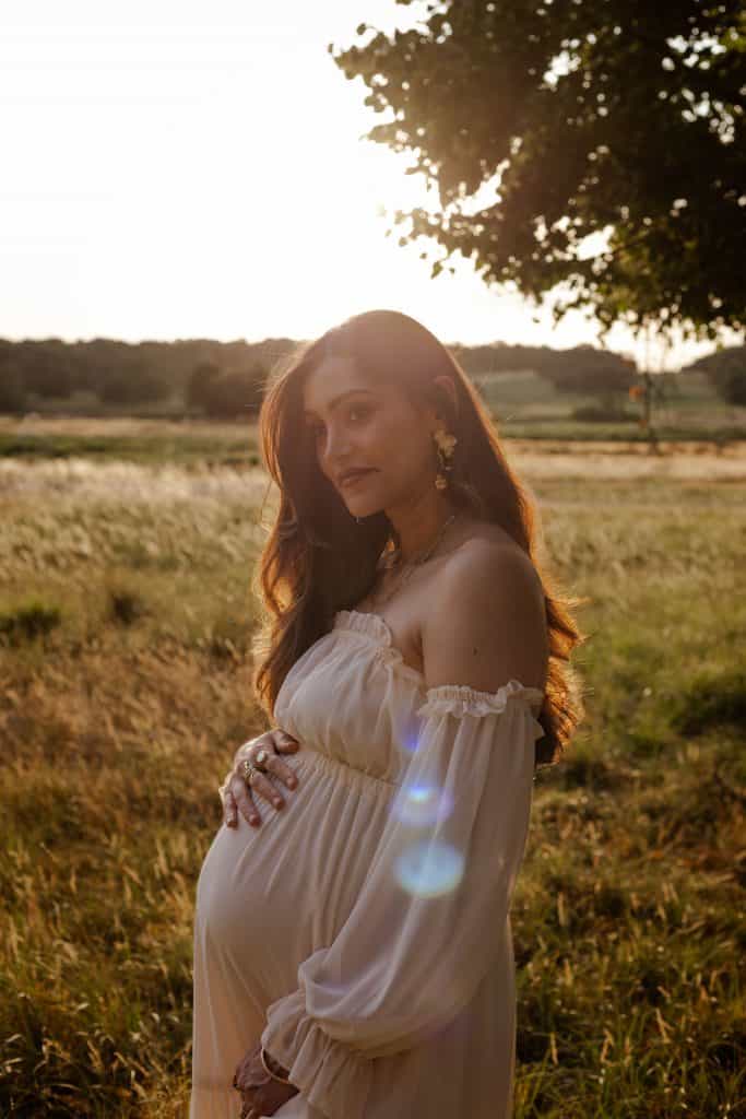 Pregnant woman in a white dress photographed in golden-hour light in a field