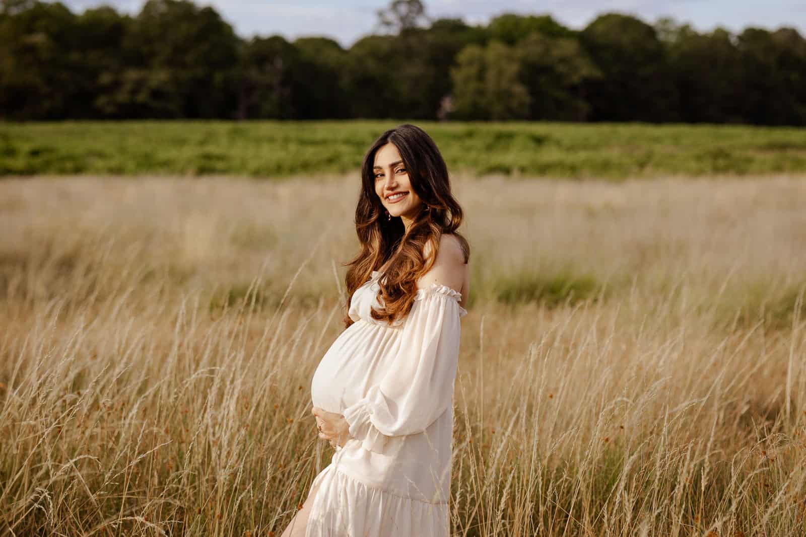 Pregnant woman in a white dress standing in a field during a maternity photography session in London