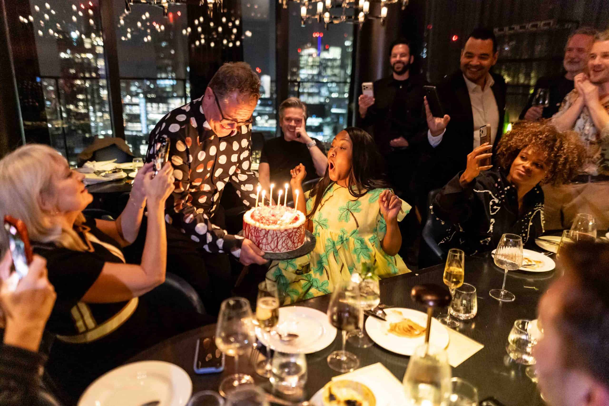 London birthday party photography capturing guests celebrating with a birthday cake at a dinner overlooking the city