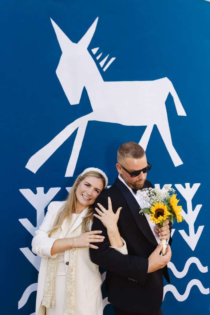 Newly married couple laughing together with a sunflower bouquet against a blue mural in London