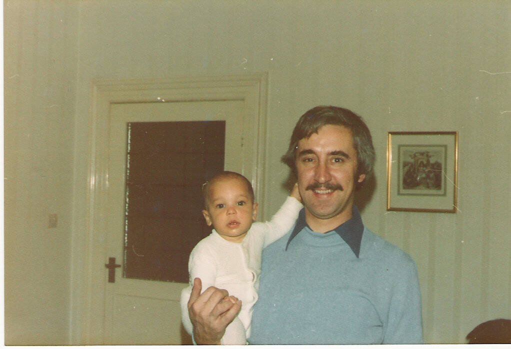 Childhood photograph of a young child being held by their father in 1978