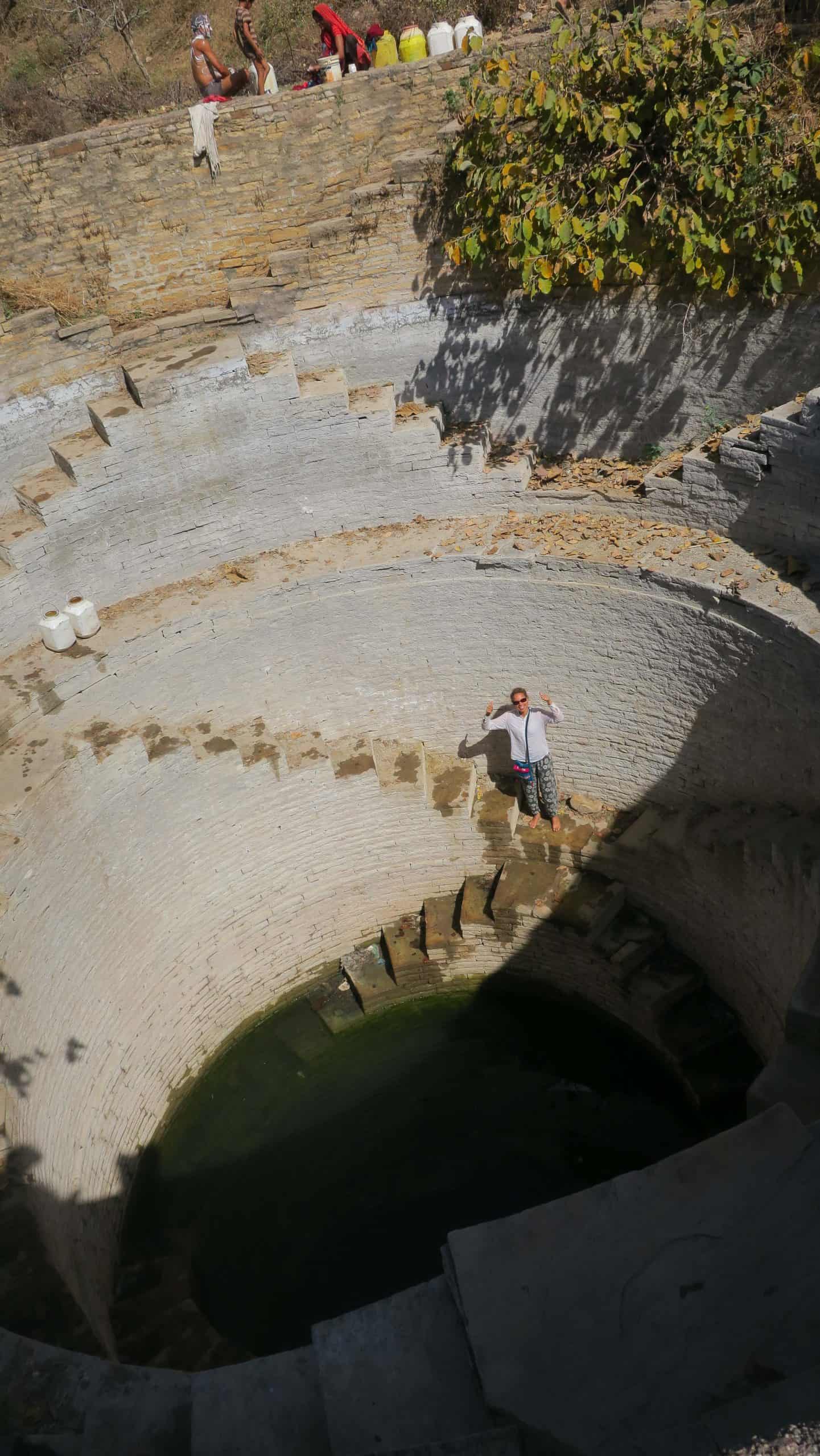 Photographer standing on the curved stone steps of an ancient Indian stepwell, surrounded by concentric levels of masonry.